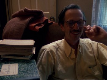 Movie still from “Crumb” (1994), directed by Terry Zwigoff – A man sitting in front of a pile of books; Medium shot, High angle