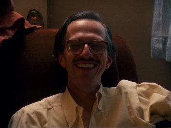 Movie still from “Crumb” (1994), directed by Terry Zwigoff – A man sitting in a chair smiling for the camera; Close Up shot, Low angle