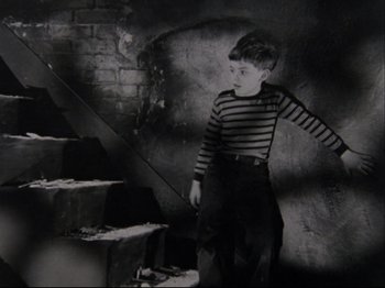 Movie still from “Crumb” (1994), directed by Terry Zwigoff – A young boy standing in front of a staircase; Medium shot, High angle