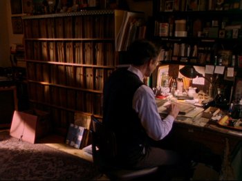Movie still from “Crumb” (1994), directed by Terry Zwigoff – A man sitting at a desk in front of papers; Wide shot, High angle