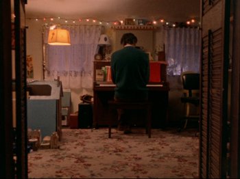 Movie still from “Crumb” (1994), directed by Terry Zwigoff – A person sitting at a piano in a room; Wide shot, High angle