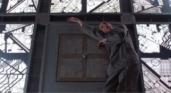 Movie still from “Cube” (1997), directed by Vincenzo Natali – A man in a gray shirt is throwing a ball; Wide shot, Low angle