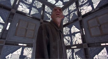 Movie still from “Cube” (1997), directed by Vincenzo Natali – A man standing inside of a building looking up; Medium shot, Low angle