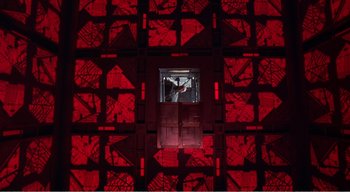 Movie still from “Cube” (1997), directed by Vincenzo Natali – A person standing in a room with a red wall; Extreme Wide shot, Overhead angle