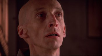 Movie still from “Cube” (1997), directed by Vincenzo Natali – A man with bald head looking up at the sky; Close Up shot, Low angle