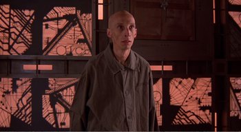 Movie still from “Cube” (1997), directed by Vincenzo Natali – A bald man standing in front of a building; Medium shot, Low angle