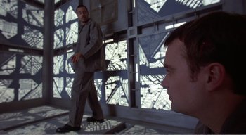 Movie still from “Cube” (1997), directed by Vincenzo Natali – A man standing next to another man on a bridge; Medium shot, Low angle