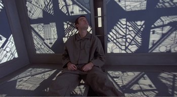 Movie still from “Cube” (1997), directed by Vincenzo Natali – A man sitting on the ground with his eyes closed; Medium shot, Overhead angle