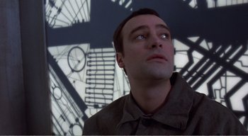 Movie still from “Cube” (1997), directed by Vincenzo Natali – A man standing in front of a wall with clocks on it; Close Up shot, Low angle
