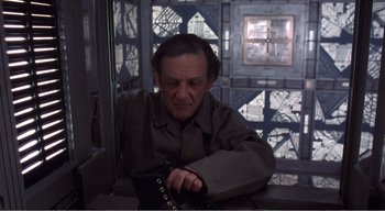 Movie still from “Cube” (1997), directed by Vincenzo Natali – An older man sitting in a room with a cell phone; Medium shot, High angle