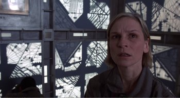 Movie still from “Cube” (1997), directed by Vincenzo Natali – A woman standing in front of a window with a building in the background; Close Up shot, Low angle