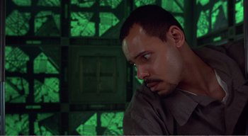 Movie still from “Cube” (1997), directed by Vincenzo Natali – A person in a room with green lights in the background; Close Up shot, High angle