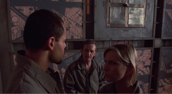 Movie still from “Cube” (1997), directed by Vincenzo Natali – A man and two women are talking to each other; Medium shot, Over the shoulder angle