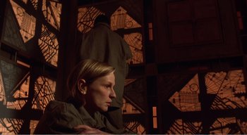Movie still from “Cube” (1997), directed by Vincenzo Natali – A woman sitting on a chair in front of a building; Medium shot, Low angle
