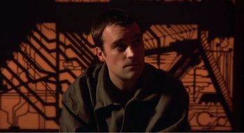 Movie still from “Cube” (1997), directed by Vincenzo Natali – A man sitting in front of an orange wall; Close Up shot, High angle