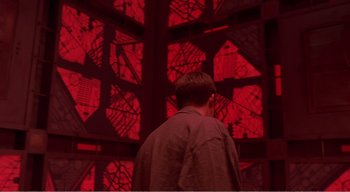 Movie still from “Cube” (1997), directed by Vincenzo Natali – A man standing in front of a wall of red lights; Medium shot, Over the shoulder angle