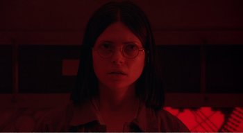 Movie still from “Cube” (1997), directed by Vincenzo Natali – A woman with glasses is in a dark room; Close Up shot, Low angle