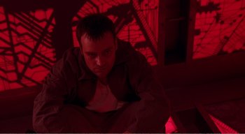 Movie still from “Cube” (1997), directed by Vincenzo Natali – A man sitting on the ground in a dark room; Medium shot, Low angle
