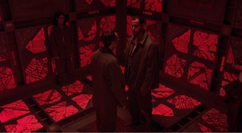Movie still from “Cube” (1997), directed by Vincenzo Natali – Two men are standing in a room with red lighting; Wide shot, High angle