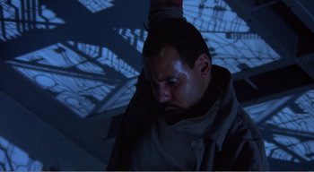 Movie still from “Cube” (1997), directed by Vincenzo Natali – A man in a dark room looking down at the ground; Close Up shot, Overhead angle