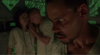 Movie still from “Cube” (1997), directed by Vincenzo Natali – A man looking at the camera while another man looks at him; Close Up shot, Low angle