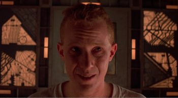 Movie still from “Cube” (1997), directed by Vincenzo Natali – A person's face in a dark room; Close Up shot, Low angle