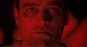 Movie still from “Cube” (1997), directed by Vincenzo Natali – A person's face in a red light; Close Up shot, Low angle
