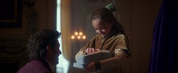 Movie still from “The Greatest Showman” (2017), directed by Michael Gracey – A young girl is holding a book while a man looks on; Medium shot, Over the shoulder angle