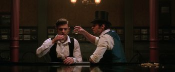Movie still from “The Greatest Showman” (2017), directed by Michael Gracey – Two men sitting at a table with a drink in front of them; Medium shot, Over the shoulder angle