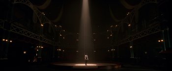 Movie still from “The Greatest Showman” (2017), directed by Michael Gracey – A man standing on a stage in the middle of a dark room; Extreme Wide shot, Low angle