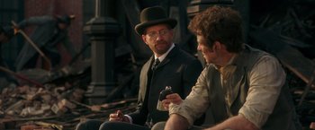 Movie still from “The Greatest Showman” (2017), directed by Michael Gracey – A man in a suit and a top hat sitting next to another man holding a phone; Medium shot, Over the shoulder angle