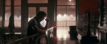 Movie still from “The Greatest Showman” (2017), directed by Michael Gracey – A man sitting at a table in front of an empty bottle; Medium shot, Over the shoulder angle