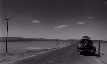 Movie still from “Cul-de-sac” (1966), directed by Roman Polanski – A black and white photo of a car on the side of the road; Extreme Wide shot, Low angle