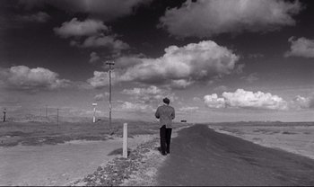 Movie still from “Cul-de-sac” (1966), directed by Roman Polanski – A man walking down a dirt road in the desert; Extreme Wide shot, High angle
