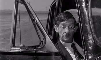 Movie still from “Cul-de-sac” (1966), directed by Roman Polanski – A black and white photo of a man in a suit and tie; Close Up shot, Over the shoulder angle