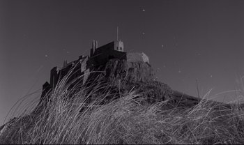 Movie still from “Cul-de-sac” (1966), directed by Roman Polanski – A black - and - white photo of a castle on top of a hill; Extreme Wide shot, Low angle