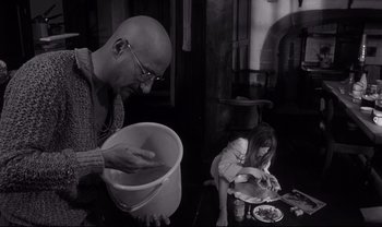 Movie still from “Cul-de-sac” (1966), directed by Roman Polanski – A man and a girl are preparing food in a kitchen; Medium shot, High angle