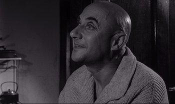 Movie still from “Cul-de-sac” (1966), directed by Roman Polanski – An older bald man wearing a robe looking to his left; Close Up shot, Low angle