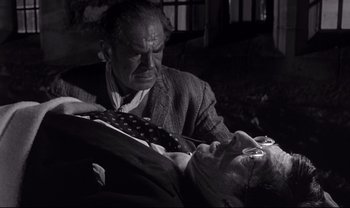 Movie still from “Cul-de-sac” (1966), directed by Roman Polanski – An older man and a younger man are sitting on a couch; Medium shot, High angle