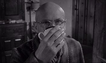 Movie still from “Cul-de-sac” (1966), directed by Roman Polanski – A bald man wearing glasses holding a coffee mug; Close Up shot, Low angle