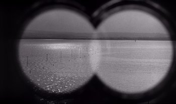 Movie still from “Cul-de-sac” (1966), directed by Roman Polanski – A black and white photo of a body of water; Extreme Wide shot, High angle