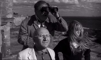 Movie still from “Cul-de-sac” (1966), directed by Roman Polanski – A man and two women looking through binoculars; Medium shot, Low angle