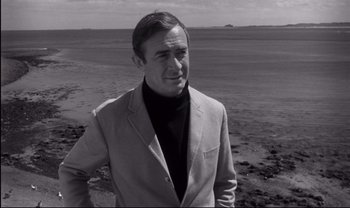 Movie still from “Cul-de-sac” (1966), directed by Roman Polanski – Black and white photograph of a man standing on the beach; Close Up shot, Over the shoulder angle