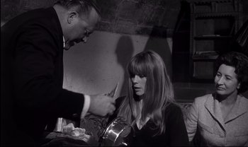 Movie still from “Cul-de-sac” (1966), directed by Roman Polanski – A man and a woman are sitting in front of a pot; Medium shot, High angle