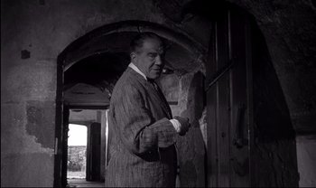 Movie still from “Cul-de-sac” (1966), directed by Roman Polanski – An older man smoking a pipe in a room; Medium shot, Low angle