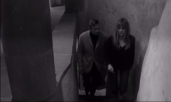 Movie still from “Cul-de-sac” (1966), directed by Roman Polanski – A man and a woman walking down a staircase; Medium shot, High angle