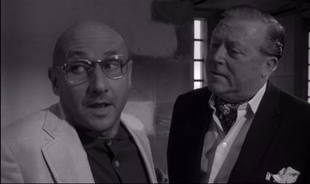 Movie still from “Cul-de-sac” (1966), directed by Roman Polanski – Two men standing next to each other in front of a brick wall; Medium shot, Over the shoulder angle