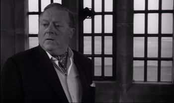 Movie still from “Cul-de-sac” (1966), directed by Roman Polanski – An older man wearing a suit and tie in front of a window; Close Up shot, Low angle