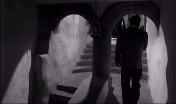 Movie still from “Cul-de-sac” (1966), directed by Roman Polanski – A man walking down a set of stairs in a building; Wide shot, High angle