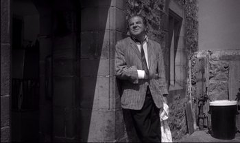 Movie still from “Cul-de-sac” (1966), directed by Roman Polanski – A black and white photo of a man leaning against a wall; Medium shot, Low angle